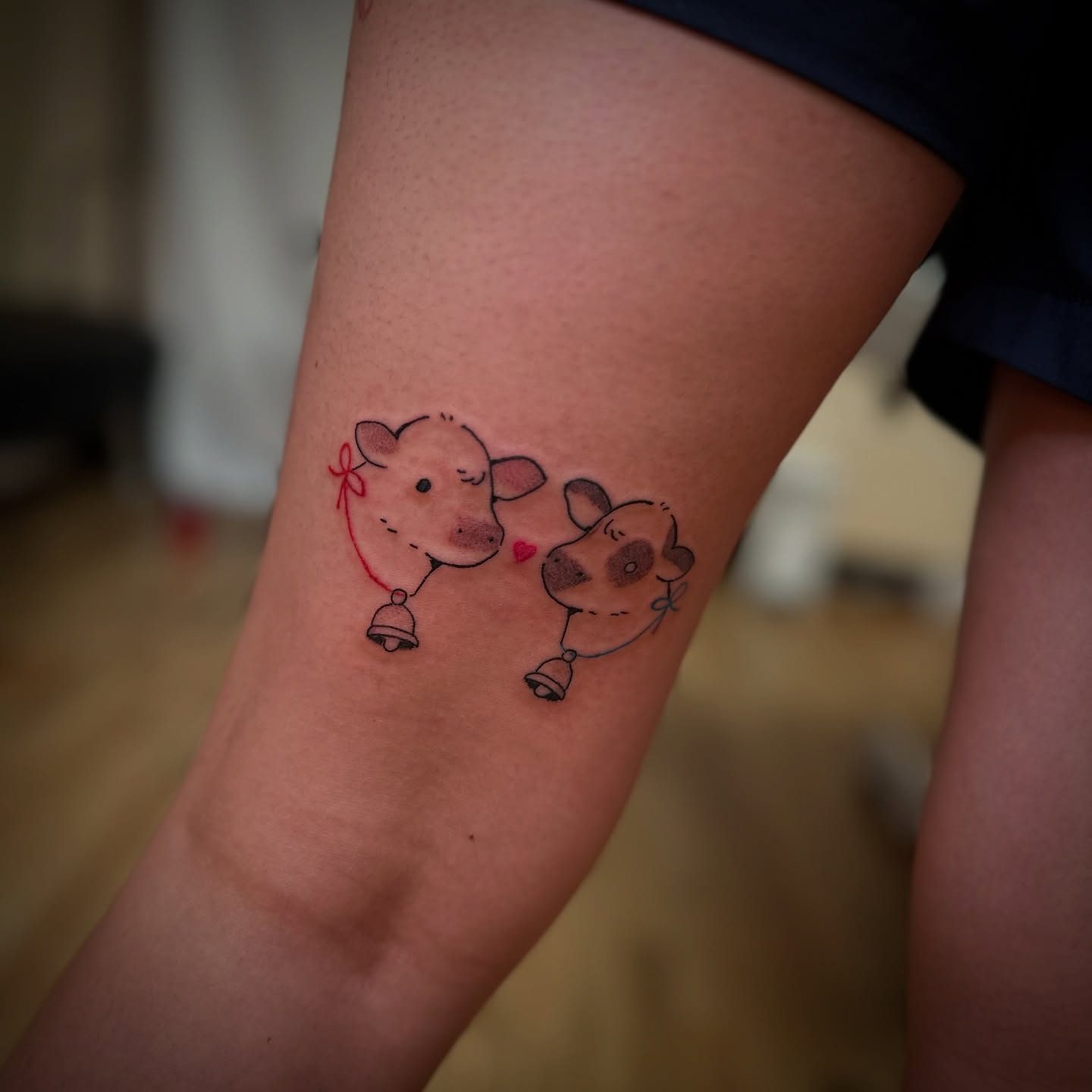 Two cow faces with cowbells, tattooed in fine line with a little colour